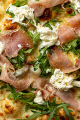 Savory homemade pizza showcases layers of creamy cheese, salty prosciutto, and fresh arugula, enticing diners in an inviting Italian restaurant ambience