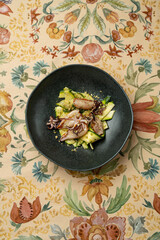 Deliciously arranged grilled squid rests atop a vibrant mix of vegetables, beautifully displayed on an artistic tablecloth in a charming restaurant. The ambiance invites a perfect dining experience