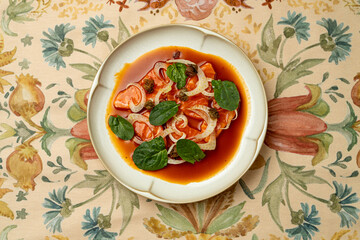 A beautiful plate of food showcases tender fish topped with juicy tomatoes, crisp onions, and fresh spinach leaves. Set on a floral tablecloth, this dish invites a delightful dining experience