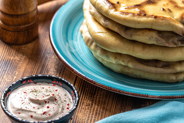 Khychins, traditional Caucasian, Eastern dish. Flatbread stuffed with minced meat with sauce on a turquoise plate with cutlery and a napkin on a wooden table. Close-up.