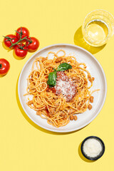 Spaghetti bolognese with tomato sauce, basil and parmesan cheese on yellow background