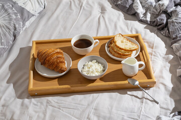 Delicious breakfast tray with croissant, bread, coffee, and cottage cheese set on a cozy bed in natural morning light