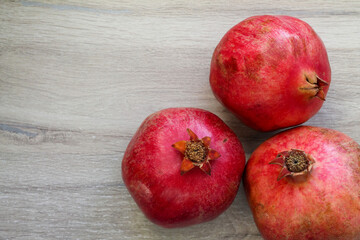 Three pomegranate fruits are lying on a wooden background, there is a free space for text on the...