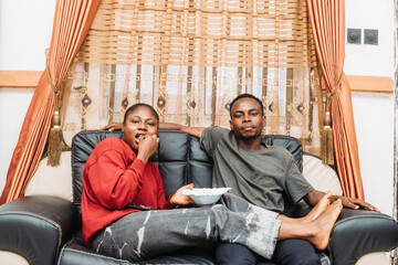 Couple Relaxing on Couch Watching TV and Sharing Snacks at Home