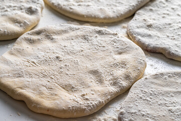 Raw Khychins, traditional Caucasian, Eastern dish. Flatbread stuffed with minced meat on a white table with flour and a rolling pin. Ready to fry.