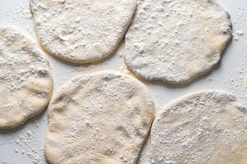 Raw Khychins, traditional Caucasian, Eastern dish. Flatbread stuffed with minced meat on a white table with flour and a rolling pin. Ready to fry.