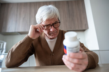 Senior man reads medicine with suspicion. Age related distrust, memory loss signs, possible dementia, medication confusion, vision correction used, home healthcare challenge, pharmaceutical hesitation