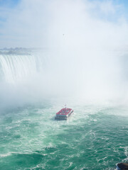 Obraz premium Niagara Falls. A pleasure boat with people near the huge famous waterfall. View from the Canadian side. Nature scenery. Photo for advertising, background, wallpaper, postcards.