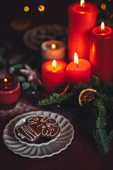 Beautiful elegant table decoration with red candles, fir tree branches with handmade craft toys in the living room. Cozy home atmosphere, holiday aesthetics, atmospheric lights, gingerbread cookies