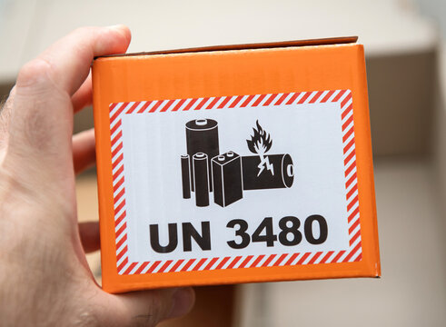 Paris, France - Apr 22, 2025: A closeup of a hand holding an orange box featuring a UN 3480 label with a warning image showing lithium batteries, one of which is on fire, indicating hazardous material