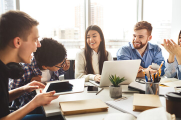Multiracial friends studying at campus library together, talking and laughing