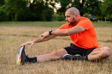 A sporty man is doing stretching exercises before running or workout outdoor in the summer park, active healthy lifestyle. 
