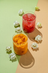 Bright and colorful drinks filled with ice sit gracefully on a vibrant surface, accompanied by soft white flowers, capturing the essence of summer refreshment and relaxation in a cozy setting
