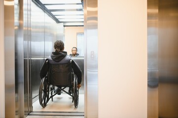 Young African American man using wheelchair entering elevator in modern building © Serhii