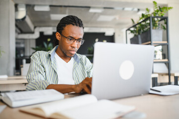 Focused university student studying on laptop in library