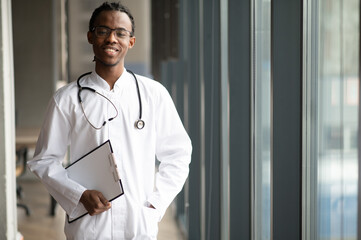 Confident young doctor standing by window