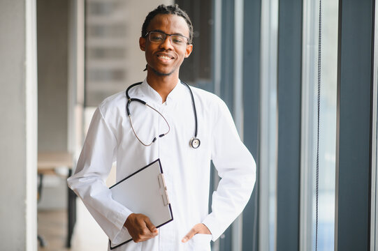 Young african american doctor smiling and holding medical chart in hospital corridor