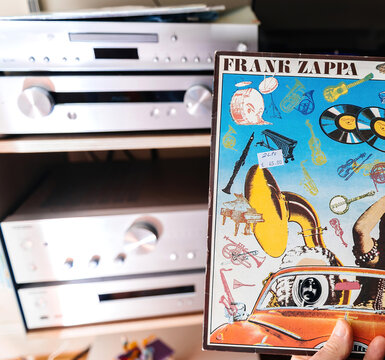 Paris, France - Feb 17, 2025: A person holds a Frank Zappa Carousel vinyl record with a colorful collage-style cover featuring musical instruments and a vintage car, with a Hi-Fi audio system
