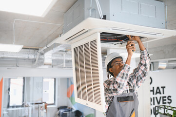 African American Skilled technician repairing office air conditioning unit
