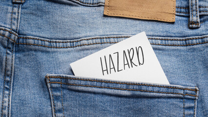 White card with a handwritten inscription "Hazard", inserted into the pocket of blue pants jeasnow (selective focus), translation: Gambling
