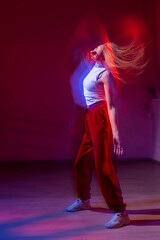 Fototapeta premium A young woman dances contemporary dances in blue and red light. Long exposure. Vertical photo. 