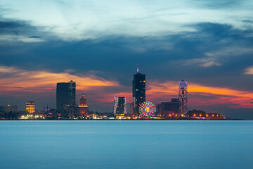 Night view of Batumi city skyline with modern buildings and a colorful illuminated ferris wheel.