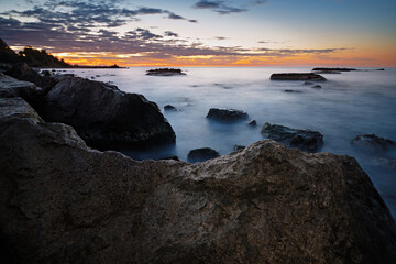 Beautiful view of the rocky seashore. Water swirls around the stones. Colorful sky. Long exposure.