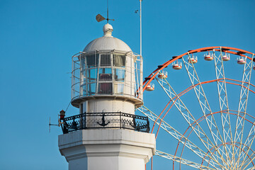 Top of a pristine white lighthouse stands beside a colorful ferris wheel in Batumi, Georgia
