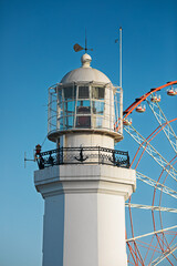 Top of a pristine white lighthouse stands beside a colorful ferris wheel in Batumi, Georgia