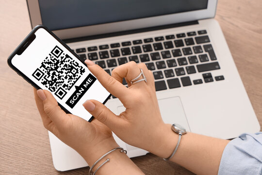 Woman holding smartphone with QR code on screen at table, closeup - Powered by Adobe