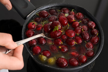 Woman preparing tasty gooseberry jam on electric stove