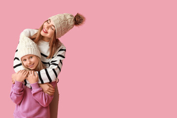 Cute little girl and her mother in warm hats on pink background
