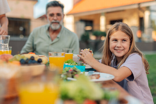 Happy girl eating burger at family lunch in garden
