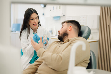 Obraz premium Dentist showing teeth model to patient in dental clinic