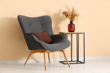 Black armchair and coffee table with pampas grass in vase near beige wall in room