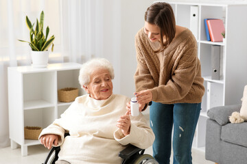 Young nurse giving pills to senior woman in wheelchair at home