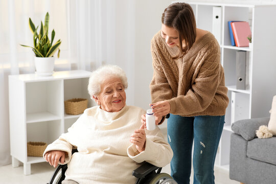 Young nurse giving pills to senior woman in wheelchair at home