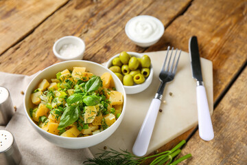 Bowl of tasty potato salad with dill and olives on wooden background