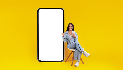 Check This. Excited lady sitting on chair using cell pointing finger at big giant smart phone with...