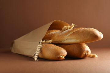 Paper bag with fresh baguettes and wheat on brown background