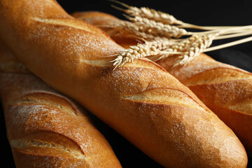 Fresh baguettes and wheat on black background, closeup
