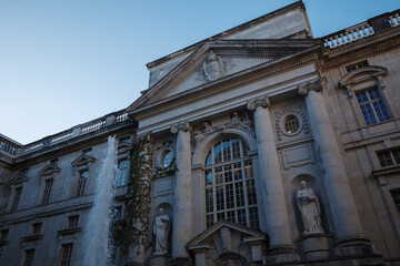 Upward view of a grand neoclassical building facade adorned with Corinthian columns, stone statues, and detailed architectural carvings at Staatsbibliothek zu Berlin. 