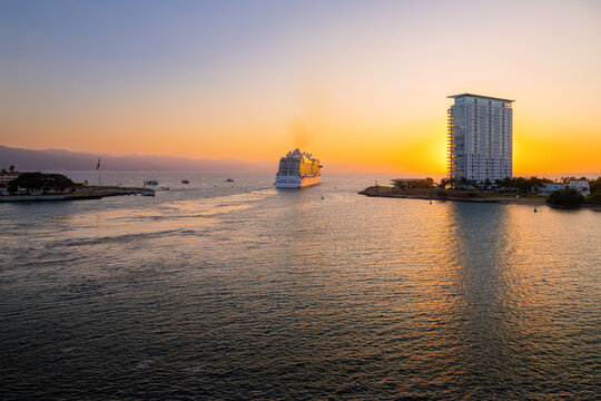 A large cruise ship reflects the sun at golden hour as it leaves the cruise port at sunset in Puerto Vallarta, Mexico.