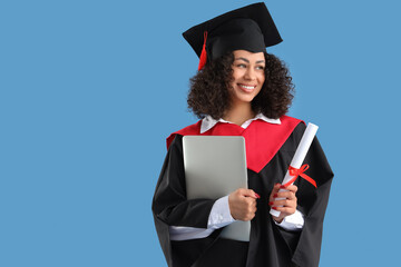 Pretty African-American female graduate with diploma and laptop on blue background