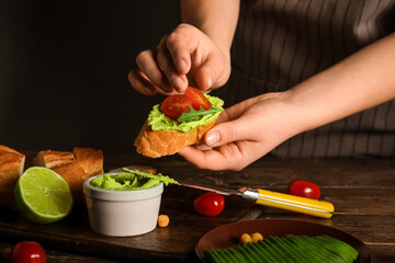 Woman preparing tasty sandwich with avocado hummus and tomatoes at wooden table, closeup