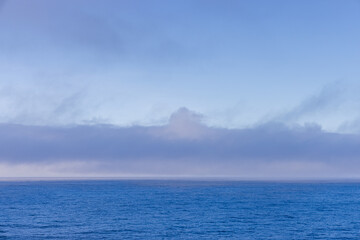 Serene Ocean View with Clouds Above the Horizon Under Clear Blue Skies