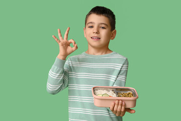 Little boy with lunchbox showing OK on green background