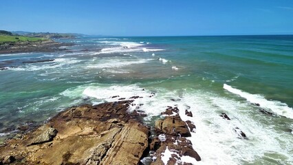 Experience the Serene Coastal Waves Rolling Upon the Rocky Shoreline Beneath Clear Blue Skies