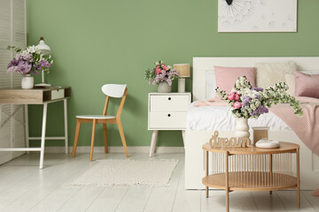 Interior of bedroom with comfortable bed, table and beautiful flowers