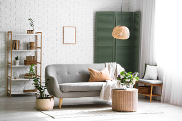 Sofa and wicker coffee table with blooming lilac branches in interior of living room